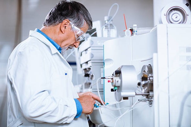 Scientist in a lab with safety equipment on using a machine to analyze molecule content.